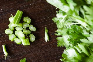 Chopped and yet-to-be-chopped stalks of celery on a dark wood cutting board.