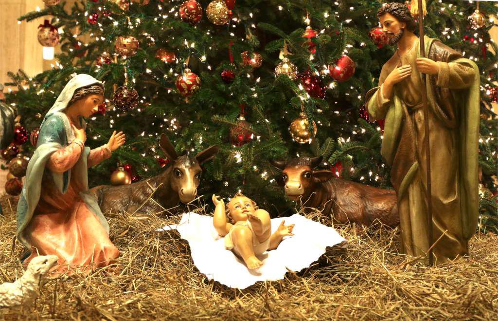 Nativity scene with Mary, Jesus and Joseph on straw under a live Christmas tree.