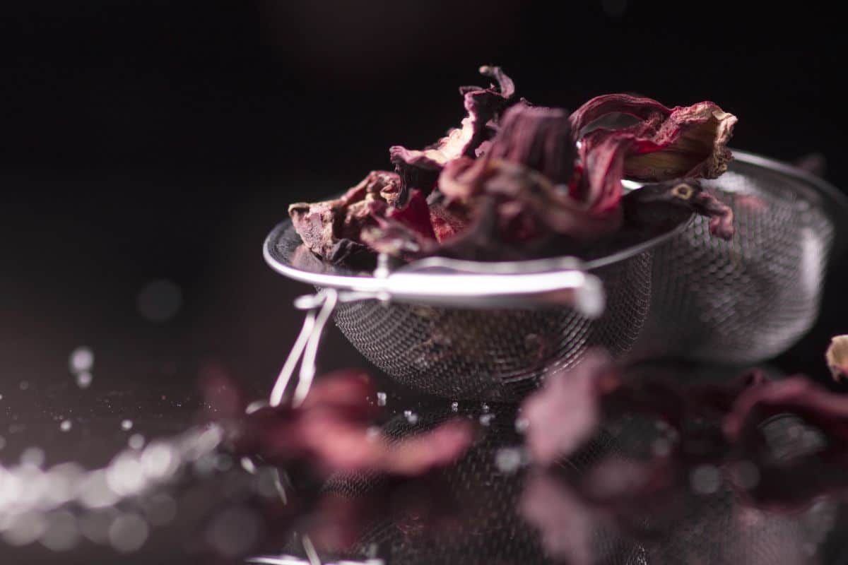 Open tea ball with dried carcade petals overflowing from it.