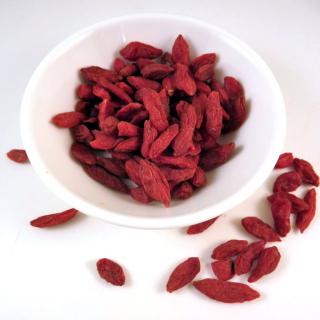 Dried red goji berries in a white bowl with a dew spilled to the side.