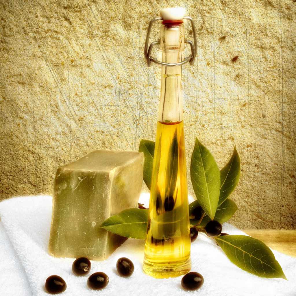 Olive soap, oil and fruits on a white towel in front of a beautiful stone wall.