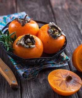 Three ripe orange persimmon fruits on a table, a fourth sliced open.