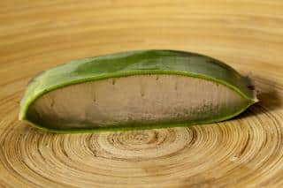 A slice of aloe vera on a wooden circular chopping board.