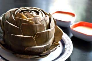 Artichoke with snipped leaves on a plate with sauces.