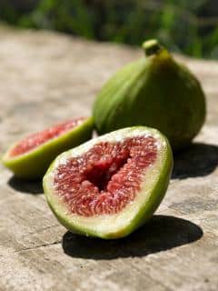 A ripe green fig sliced open on a wooden outdoor table.
