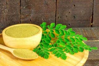 Moringa leaf and powder in bowl and spoon on a wooden tray