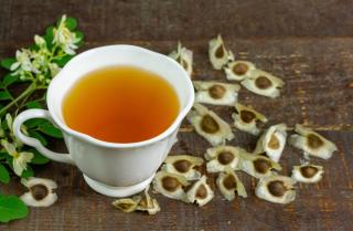 Moringa tea in a cup with seeds and a flowering twig