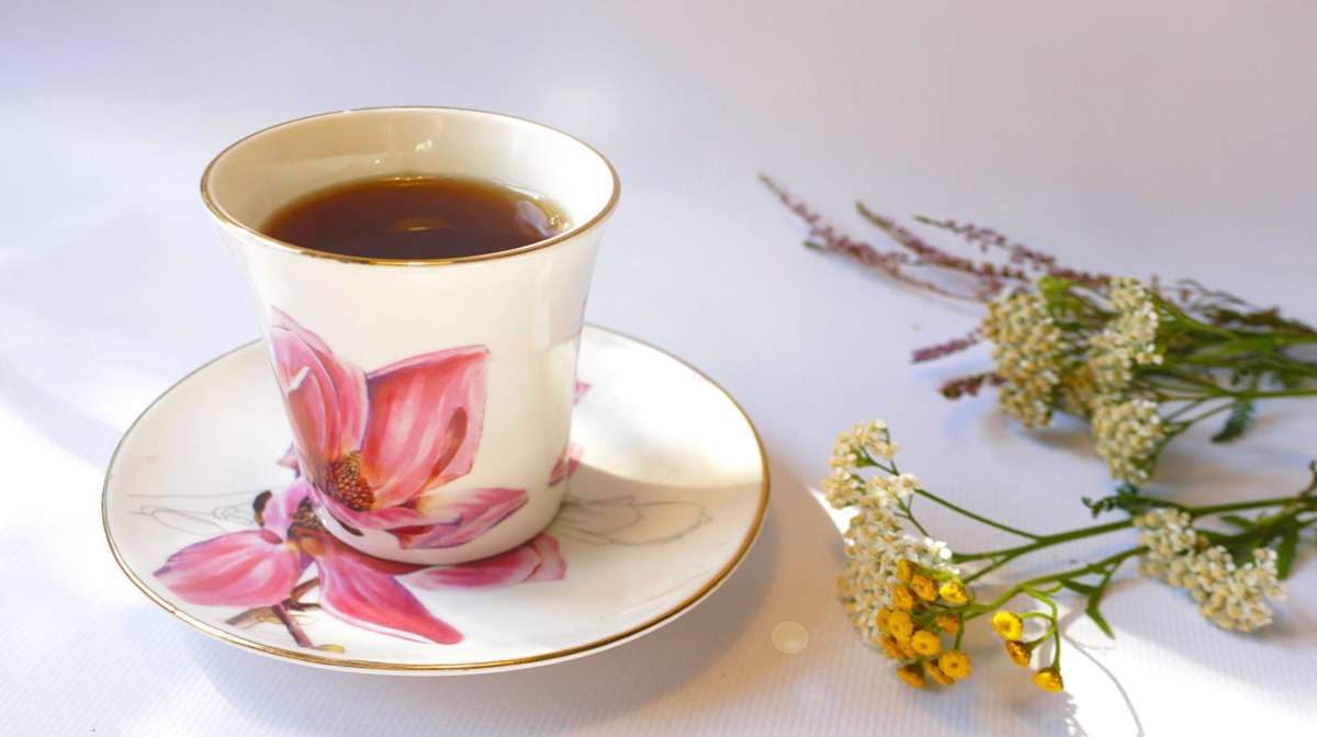 Teacup with yarrow infusion and achillea flowers on the side