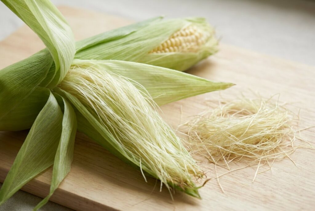 Opened maize husk showing pale gold silky styles, with a loose handful beside it